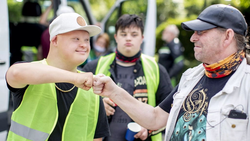 Ein Mann mit Downsyndrom begrüßt einen anderen Mann freundschaftlich mit einem Faust-Gruß. Beide gehören zu einem Motorradclub.