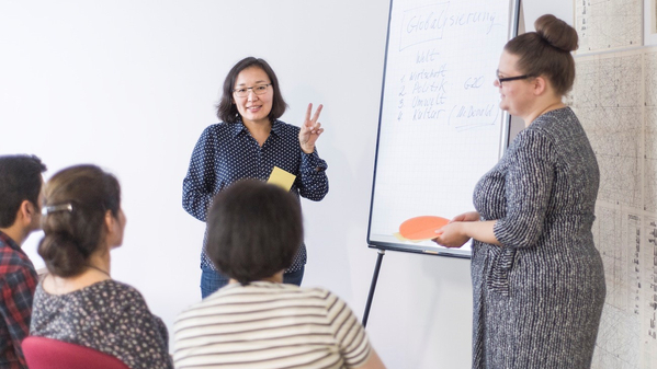 Zwei Frauen stehen vor einem Flipchart und halten einen Vortrag vor Publikum.