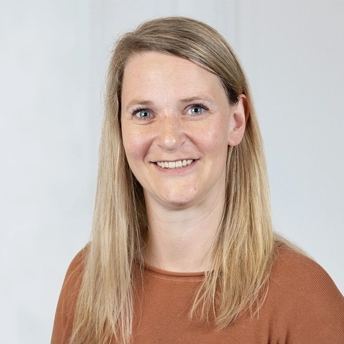 Porträt einer Frau mit langen blonden Haaren, die freundlich in die Kamera lächelt.