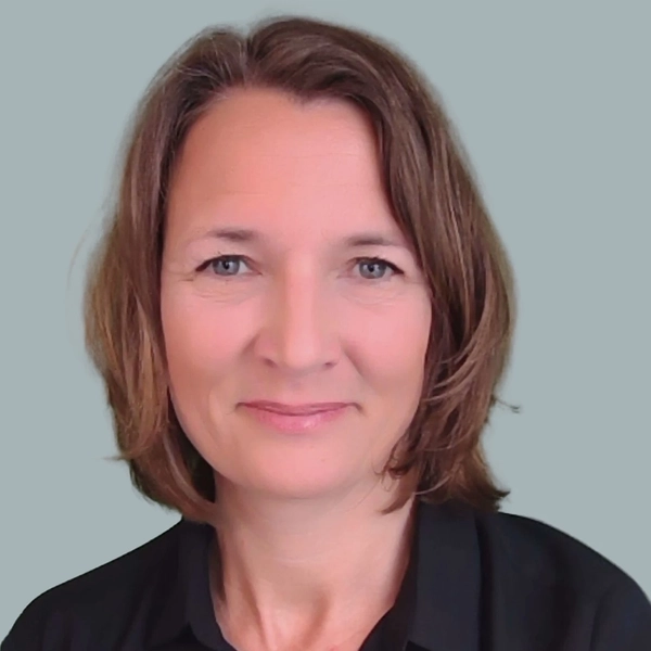 Porträt einer Frau mit schulterlangem Haar und dunkler Bluse.  Sie lächelt in die Kamera.