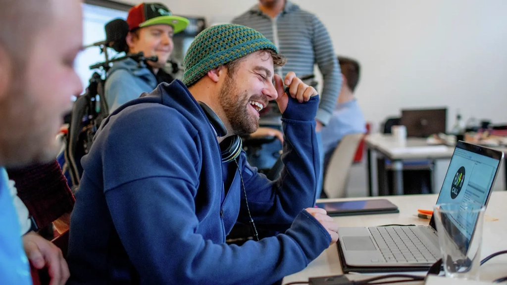 Ein Mann sitzt an einem Laptop und lacht.