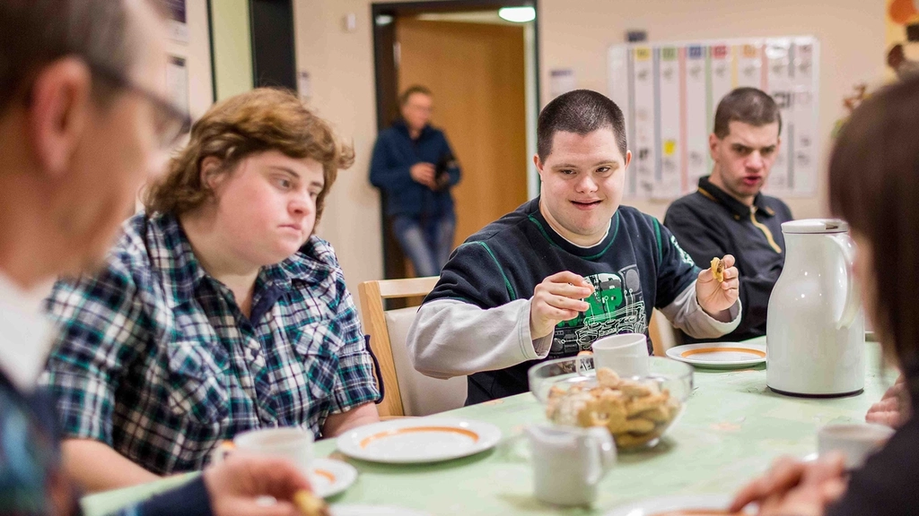 Menschen mit und ohne Behinderung sitzen beim Essen am Tisch.