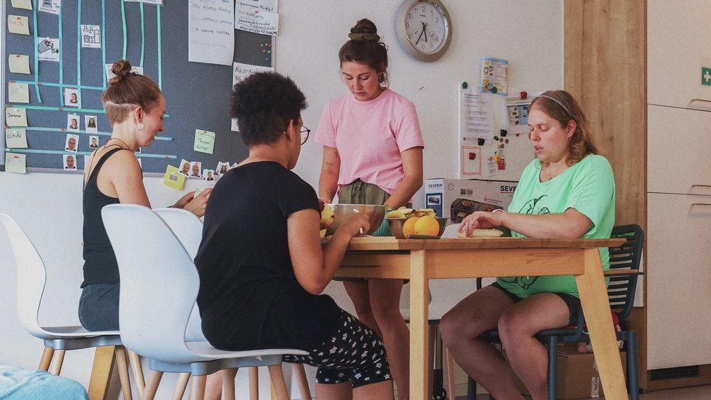An einem Esstisch in einer Wohnküche sitzen vier Personen und schneiden Gemüse.