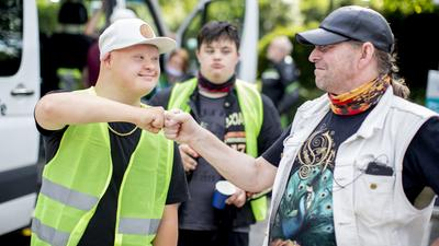 Ein Mann mit Downsyndrom begrüßt einen anderen Mann freundschaftlich mit einem Faust-Gruß. Beide gehören zu einem Motorradclub.