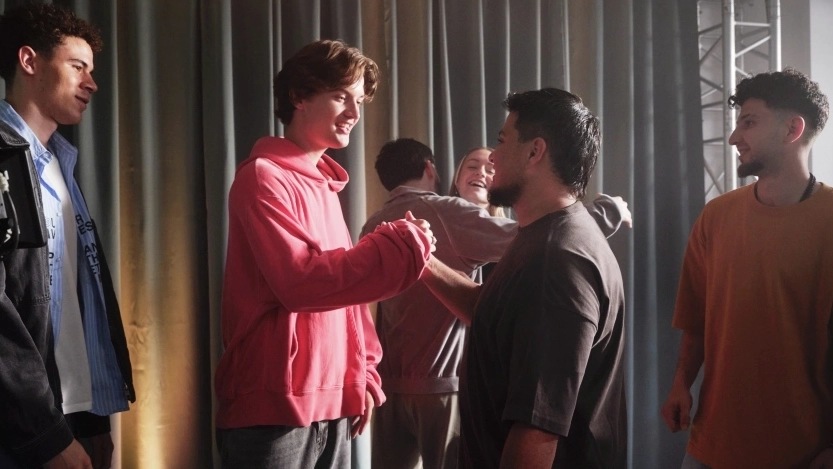 Eine Gruppe Jugendlicher steht auf einer Theaterbühne. Im Vordergrund schlagen zwei von ihnen freundschaftlich miteinander ein.