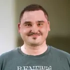 Porträtfoto von Felix. Ein Mann mit kurzem dunklem Haar im T-Shirt.