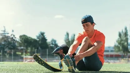 Junger Mann mit in Sportkleidung und mit Cappy sitzt auf dem Boden und bindest sich den Schuh. Am rechten Bein hat er eine Unterschenkelprothese