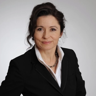 Birgit Eiber, eine Frau mittleren Alters mit dunklen Haaren, trägt einen Hosenanzug und lächelt in die Kamera.