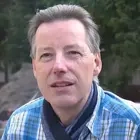 Porträt eines Mannes mit kurzem grauem Haar und blau-kariertem Hemd.