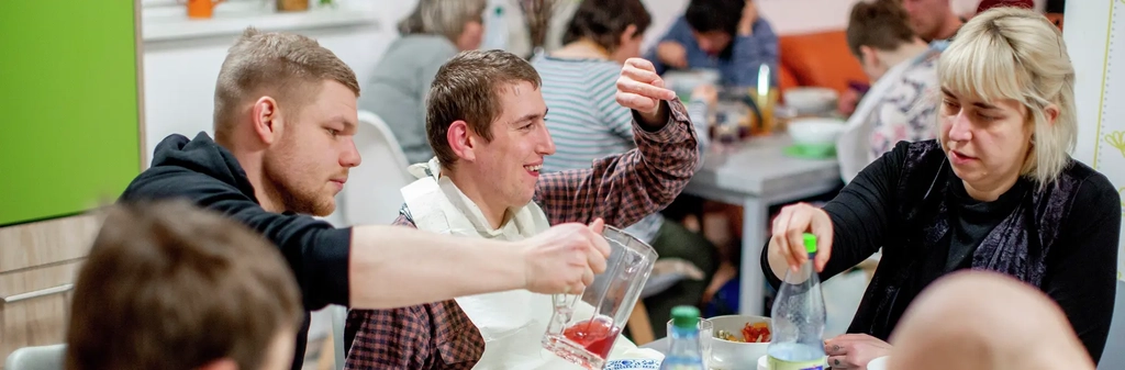Frauen und Männern  mit und ohne Behinderung sitzen beim gemeinsamen Essen am Tisch.