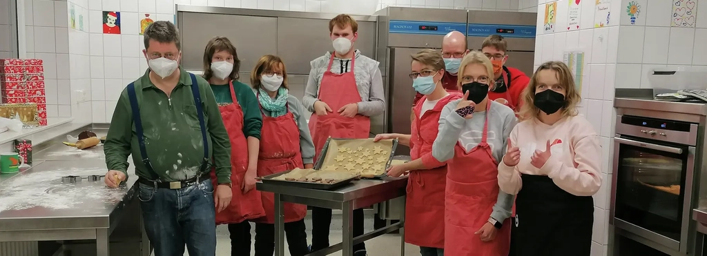 Gruppenbild von Personen, die mit Masken in einer Küche stehen und gebackene Plätzchen zeigen