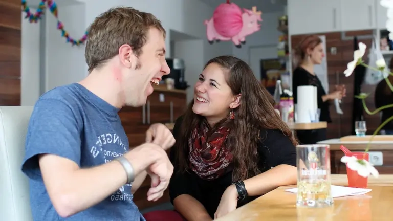 Ein Mann und eine Frau sitzen am Esstisch und lachen gemeinsam.