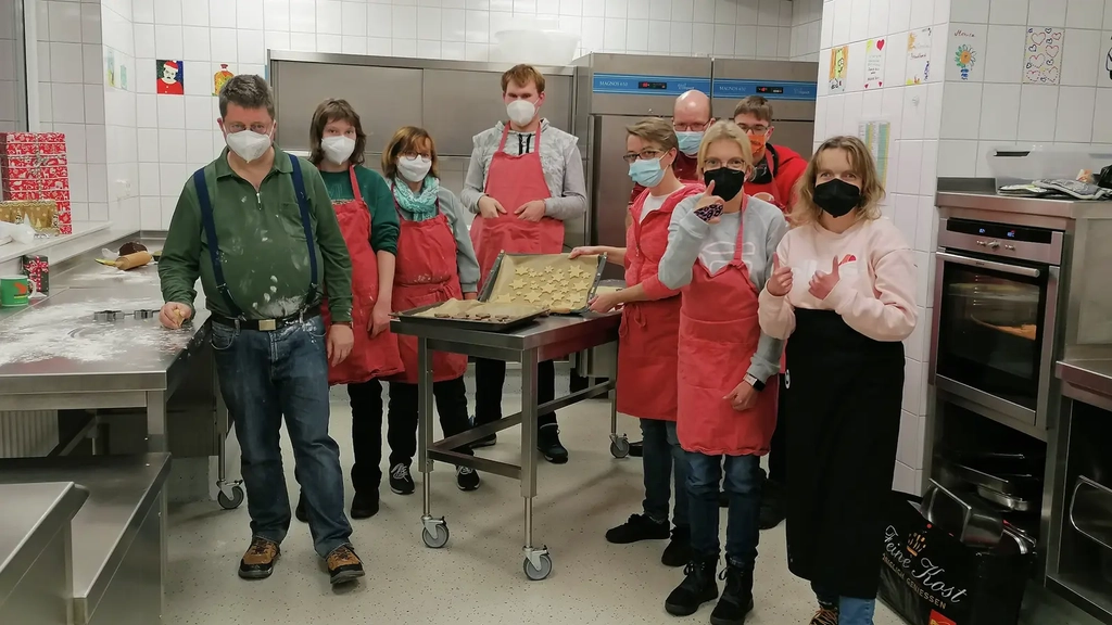 Gruppenbild von Personen, die mit Masken in einer Küche stehen und gebackene Plätzchen zeigen