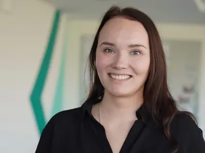 Porträt von Nadine Greve. Sie trägt dunkles langes Haar und eine schwarze Bluse. Sie lächelt.