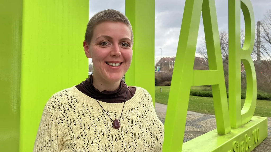 Eine Frau mit kurzem blondem Haar und hellem Strickpulli lächelt in die Kamera.