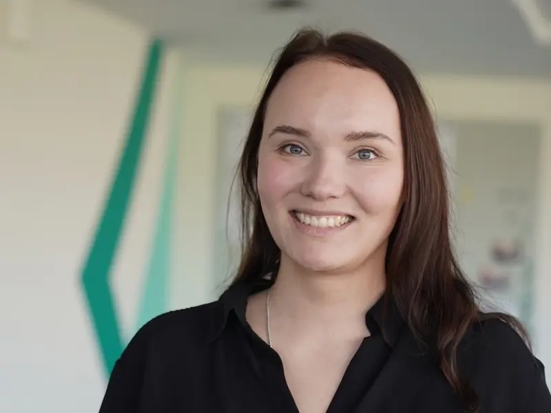 Porträt von Nadine Greve. Sie trägt dunkles langes Haar und eine schwarze Bluse. Sie lächelt.