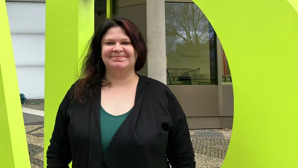 Eine Frau mit dunklem langen Haar steht vor einem großen IAB-Schriftzug.