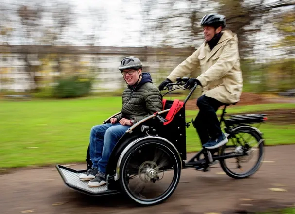 Ein Mann sitzt vorne in der Elektro-Rikscha. Ein weiterer Mann fährt die Rikscha.