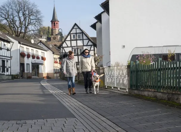 Zwei Frauen, eine mit Blindenhund, laufen eine Straße entlang