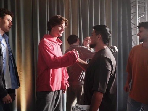 Eine Gruppe Jugendlicher steht auf einer Theaterbühne. Im Vordergrund schlagen zwei von ihnen freundschaftlich miteinander ein.