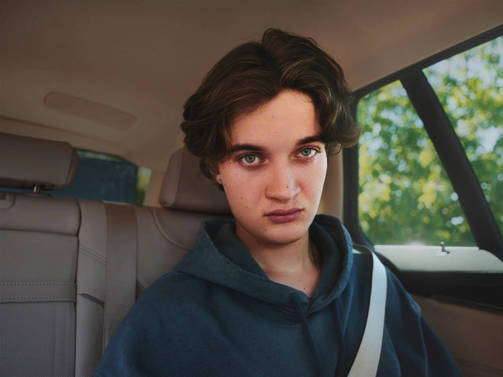 Ein junger Mann sitzt in einem Auto und schaut mit intensivem Blick in die Kamera. Seine Gesichtszüge sind ernst.