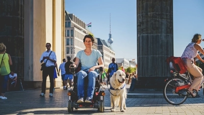 Eine Frau im Rollstuhl mit Hund in einer Straßenszene in Berlin