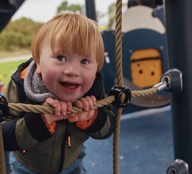 Ein Kind hält sich an den Seilen eines Klettergerüstes fest und lächelt in die Kamera.