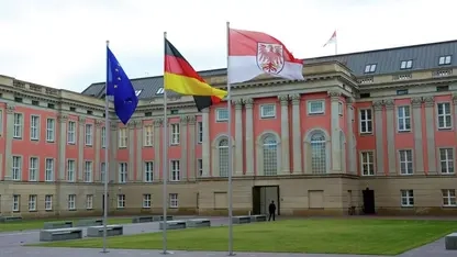 Blick vom Innenhof mit Rasen auf die Rückseite des Schlosses, in dem der brandenburgische Landtag sitzt. Im Vordergrund drei Fahnenmasten mit den Flaggen der EU, von Deutschland und Brandenburg