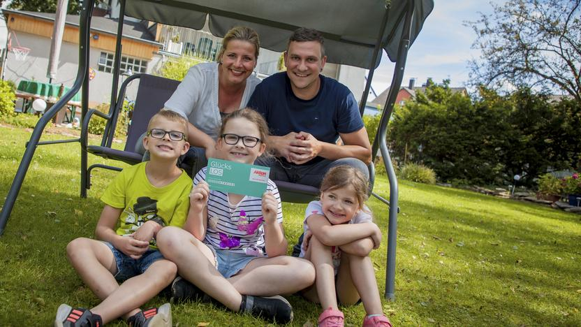 Eine Familie mit drei Kindern sitzt im Garten in einer Hollywood-Schaukel.