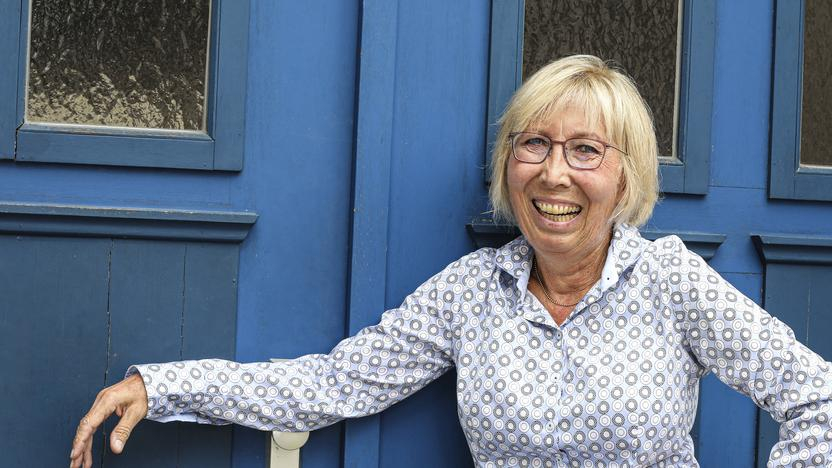 Eine blonde Frau mit Brille steht lachend vor einer blau gestrichenen Tür.