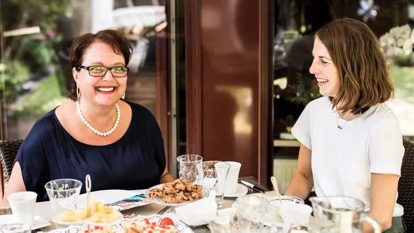 Zwei Frauen sitzen an einem Esstisch, der mit Kuchen und Keksen angerichtet ist.