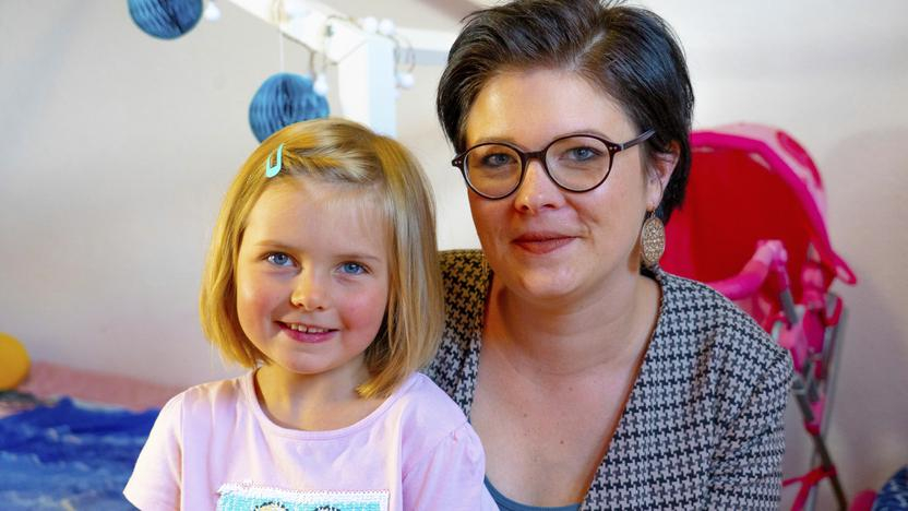 Rebecca hat ihre kleine Tochter auf dem Schoß, beide lächeln in die Kamera.