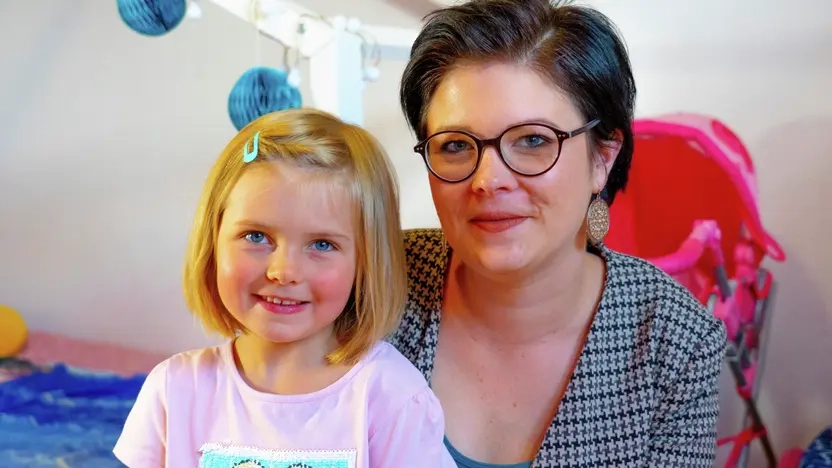 Rebecca hat ihre kleine Tochter auf dem Schoß, beide lächeln in die Kamera.