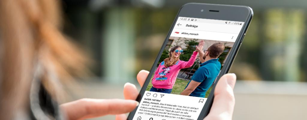 Eine Frau hält ein Smartphone in der Hand, auf dem der Instagram-Account der Aktion Mensch aufgerufen ist.
