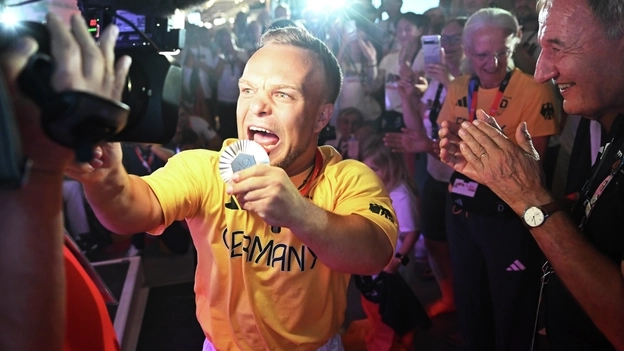 Der Para Kugelstoßer Niko Kappel präsentiert seine Medaille in Richtung einer Fernsehkamera im Deutschen Haus Paralympics in Paris 2024.
