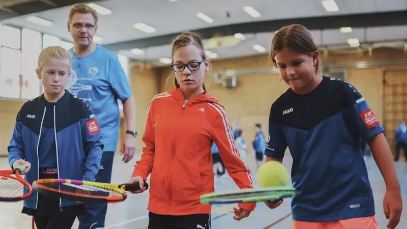 Drei Mädchen balancieren Tennisbälle auf Tennisschlägern.