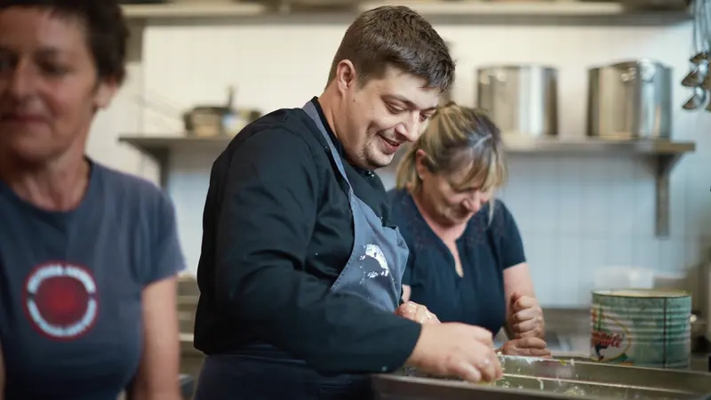 Ein Mann und zwei Frauen stehen in einer Küche und bereiten Speisen zu.