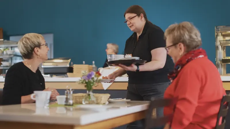 Eine junge Frau serviert  zwei Frauen, die an einem Tisch sitzen, Kaffee.