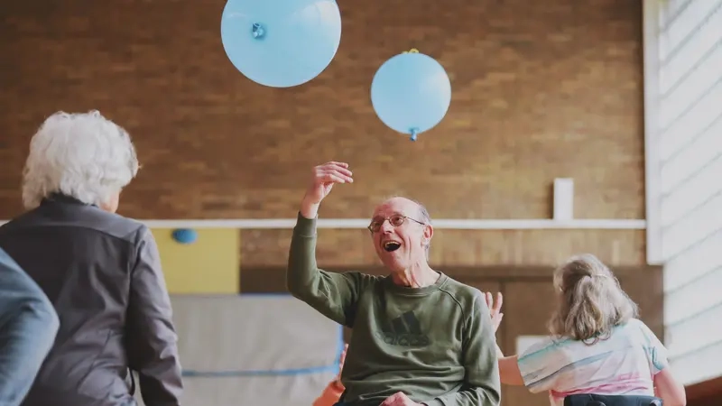 Ein Mann im Rollstuhl stößt mit seiner rechten Hand einen blauen Ballon in die Luft.