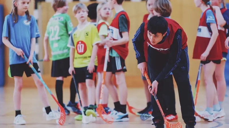 Eine Gruppe Kinder steht in einer Turnhalle vor einem Tor und hat Floorball-Schläger in den Händen.