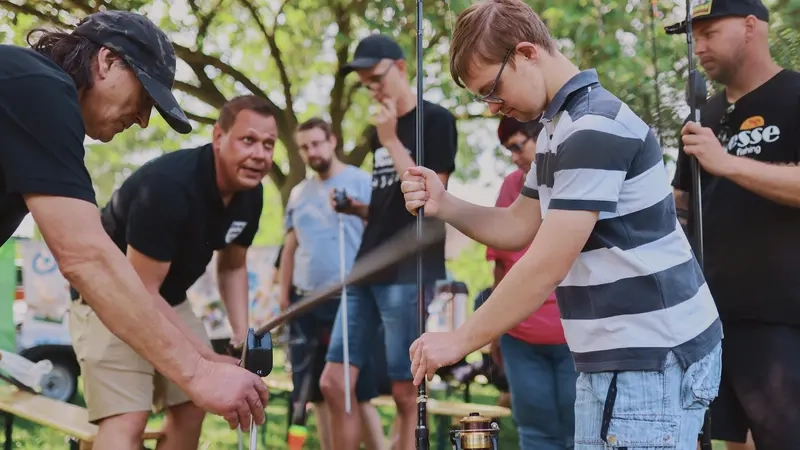 Sechs Menschen mit und ohne Behinderung stehen mit Angeln in den Händen auf einer Wiese.