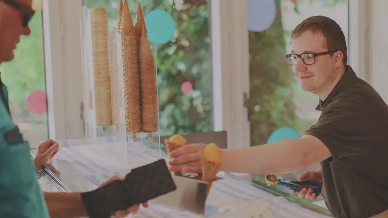 Ein Mann steckt eine Eiswaffel mit einer gelben Eiskugel in einen kleinen Ständer.