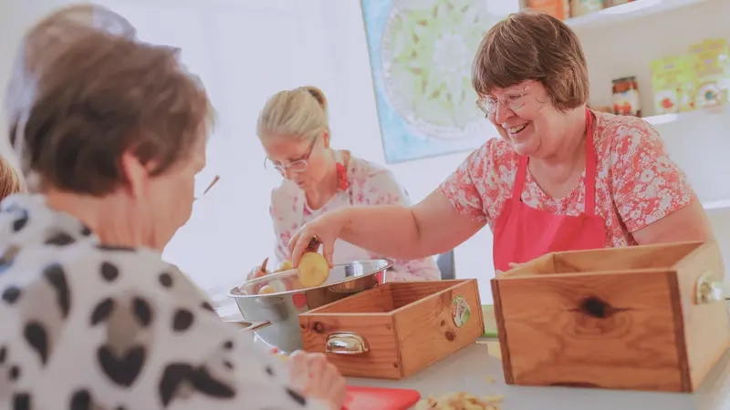 Drei Frauen sitzen an einem Glastisch und schälen Kartoffeln.