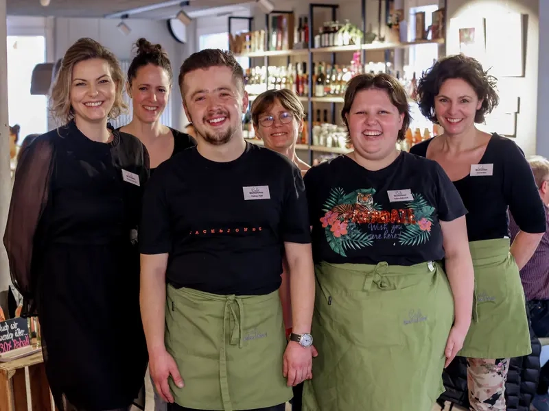 Eine Gruppe Menschen steht  vor eine Theke, sie tragen Schürzen. 