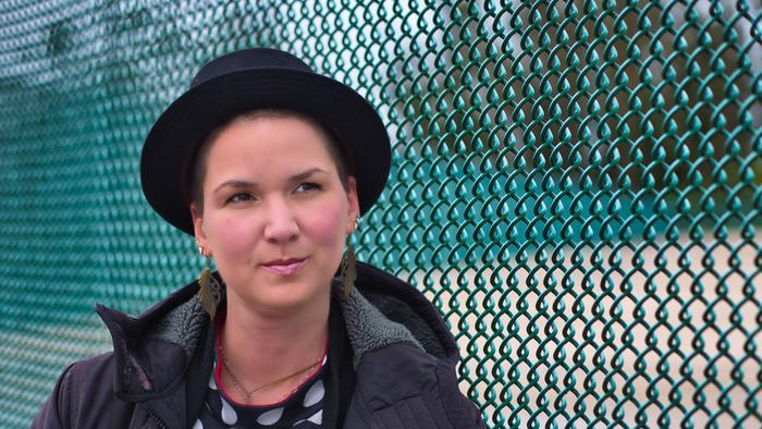 Eine Frau mit einem schwarzen Hut steht vor einem Zaun