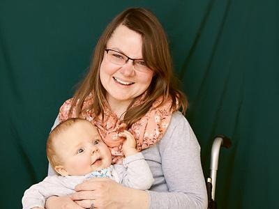 Eine Frau mit Brillen im Rollstuhl hält ein Baby auf ihrem Schoß
