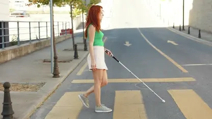 Eine Frau, die den smarten Blindenstock WeWalk benutzt, geht über einen Zebrastreifen.