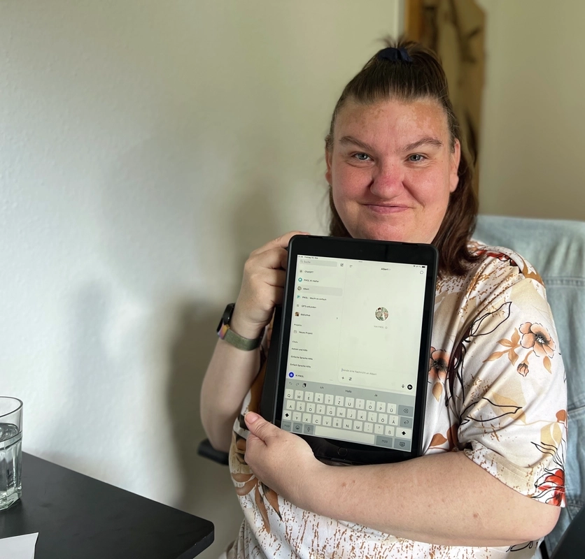Eine junge Frau hält ein Tablet in den Armen und lächelt in die Kamera.
