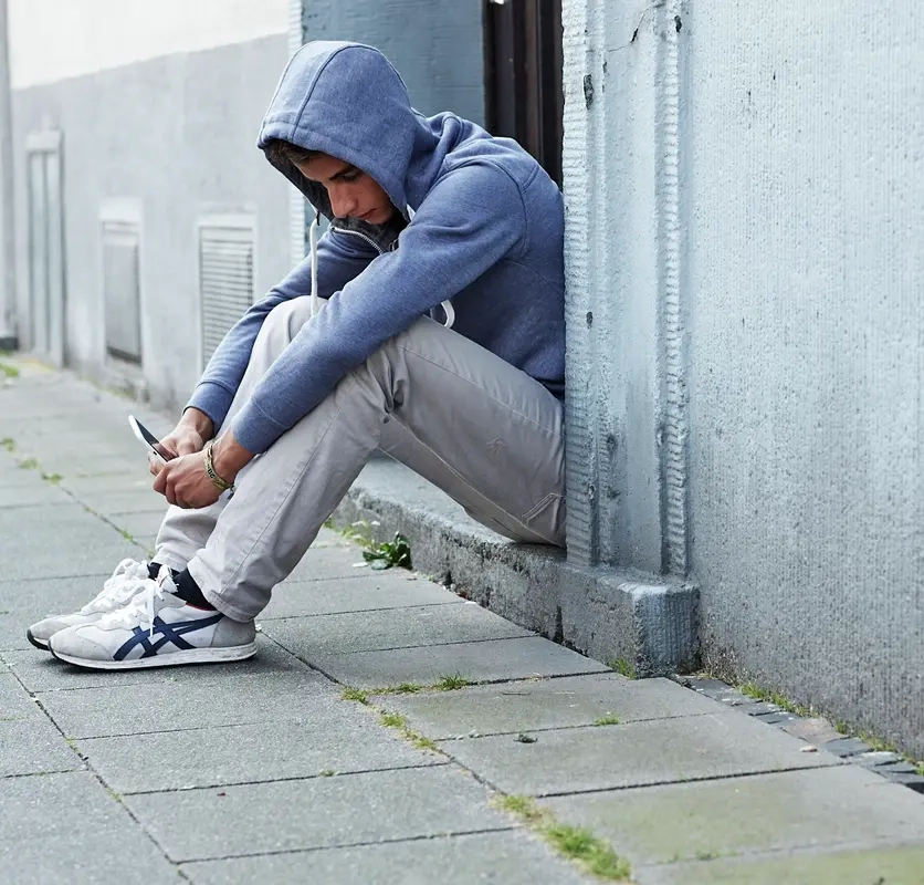 Ein Jugendlicher sitzt in einem Hauseingang und schaut auf sein Handy.