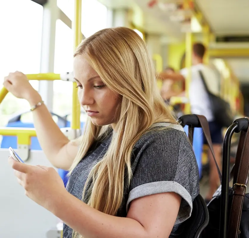 Eine junge Frau im Rollstuhl befindet sich im Bus und schaut auf ihr Smartphone.
